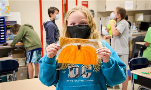 Girl holds up pumpkin painting
